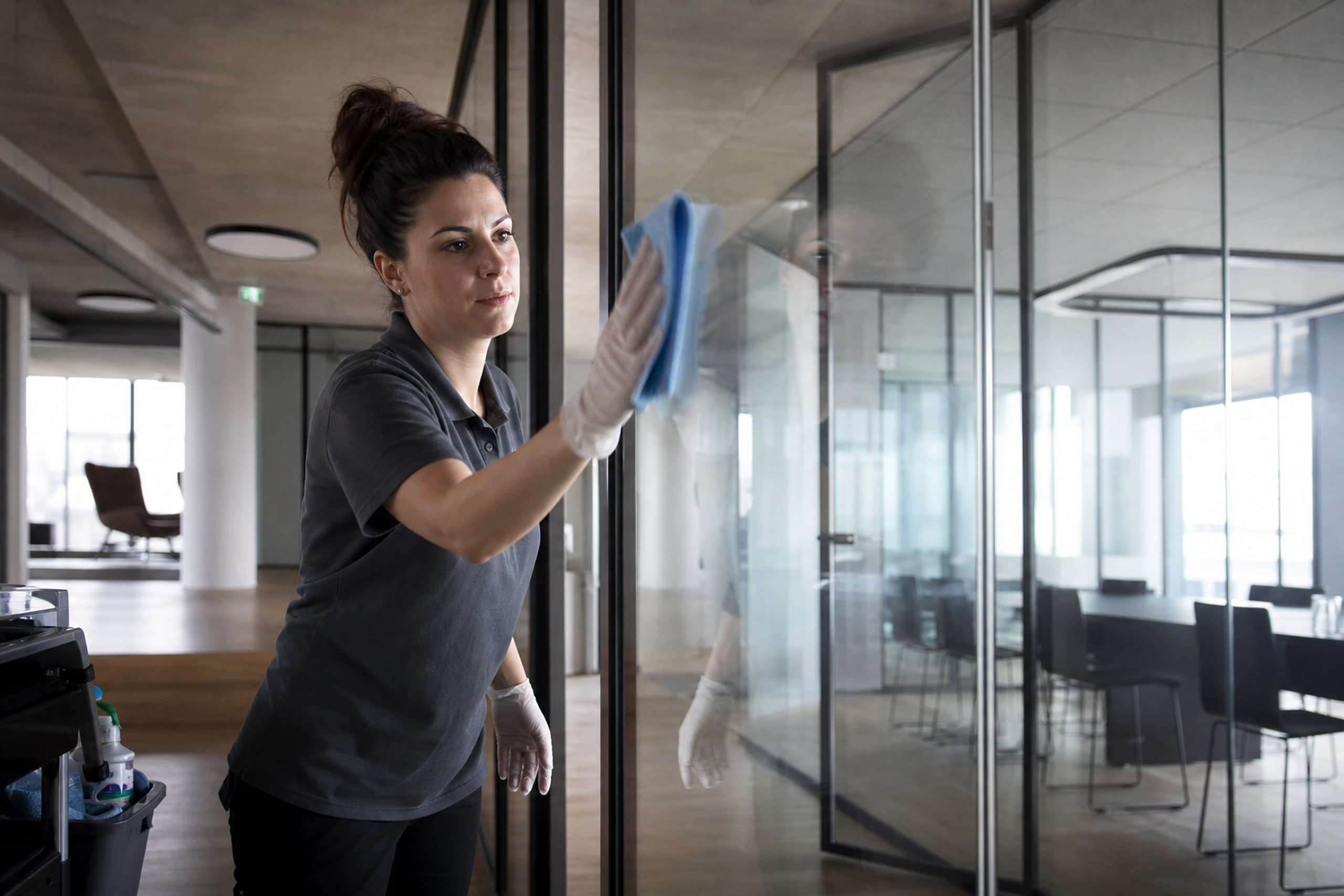 Reinigungskraft der alfin GmbH reinigt eine Glastrennwand in einem hellen Büro in Quickborn