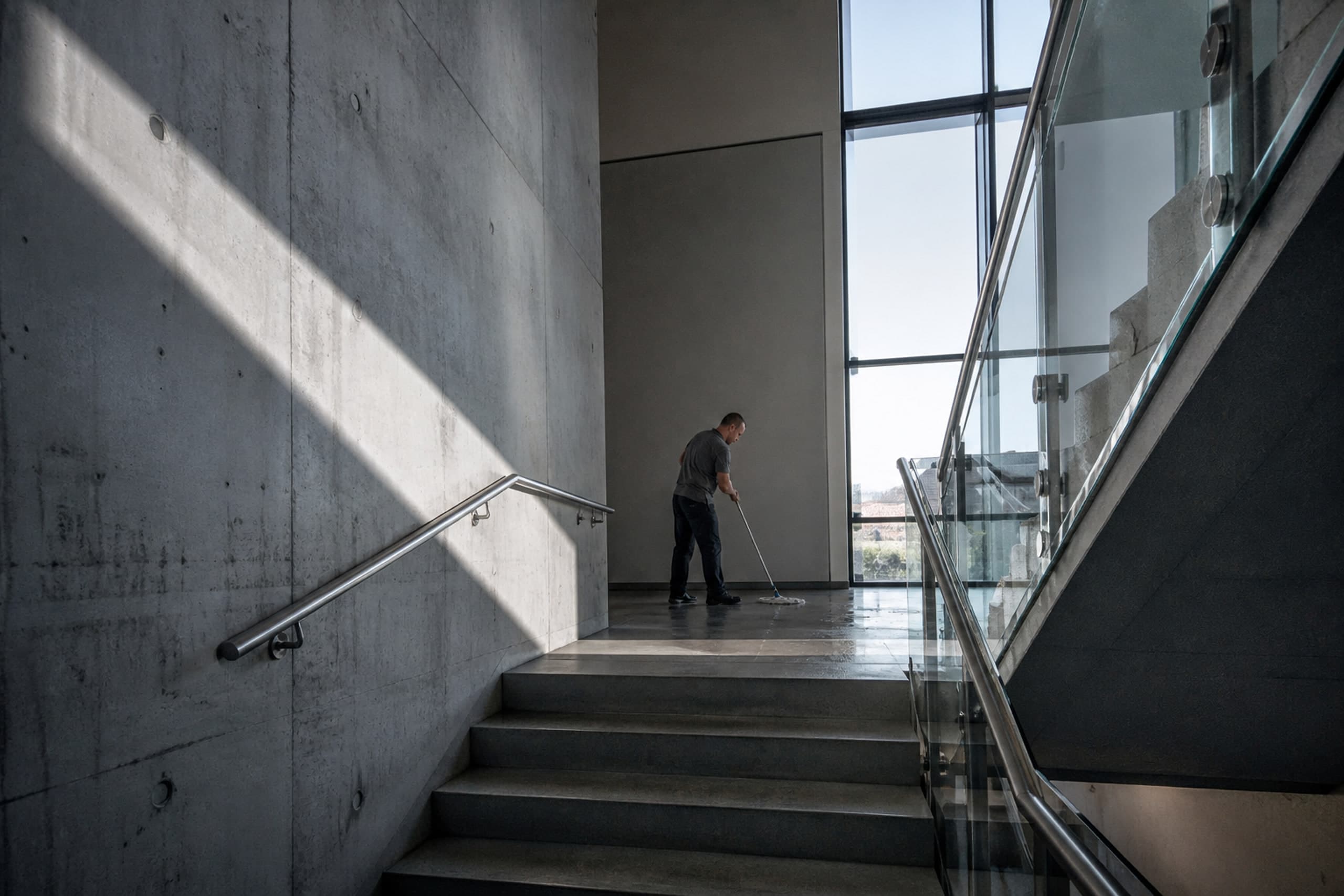 Reinigungskraft wischt ein Treppenpodest in einem hellen Betontreppenhaus
